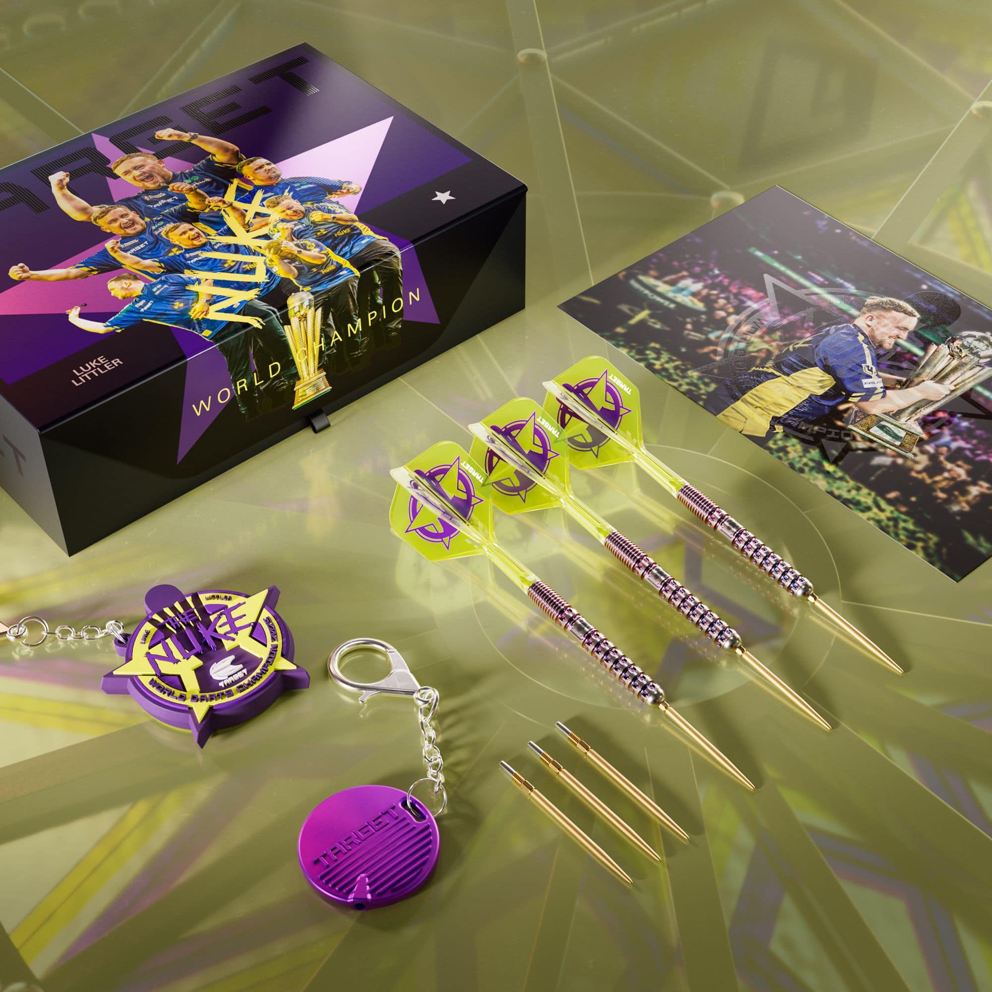 Das Bild zeigt ein Set von Steeldarts samt Zubehör und einer dekorativen Box mit dem Aufdruck "World Champion". Im Set sind außerdem eine Autogrammkarte, Ersatzspitzen und zwei Schlüsselanhänger enthalten.