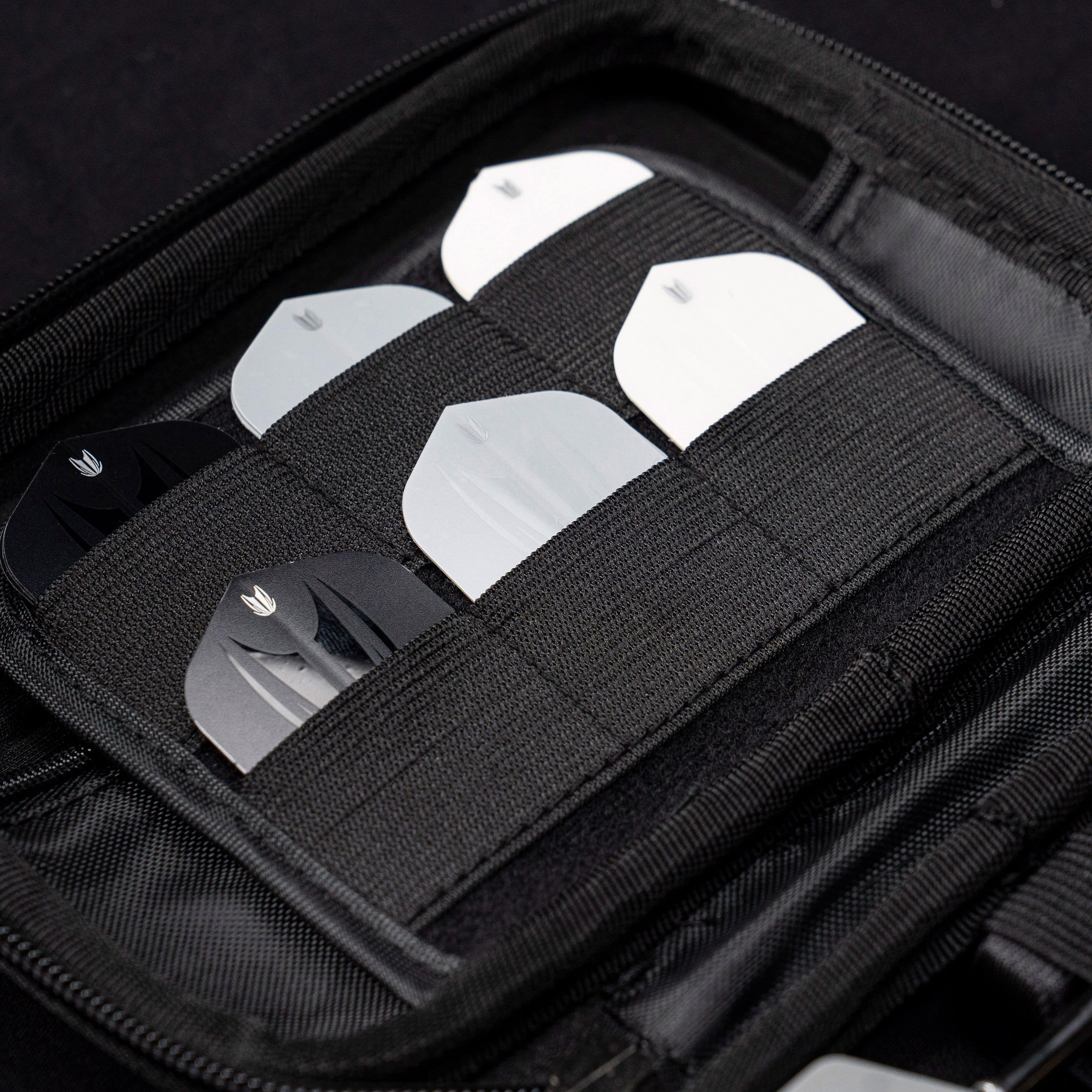 Takoma Ghost Series Nathan Aspinall darthoesje Das Bild zeigt das Target Takoma Bolide Dartcase, in dem mehrere Dart-Flights ordentlich in elastischen Halterungen verstaut sind. Das Case ist schwarz und bietet sicheren Schutz für das Dartzubehör.