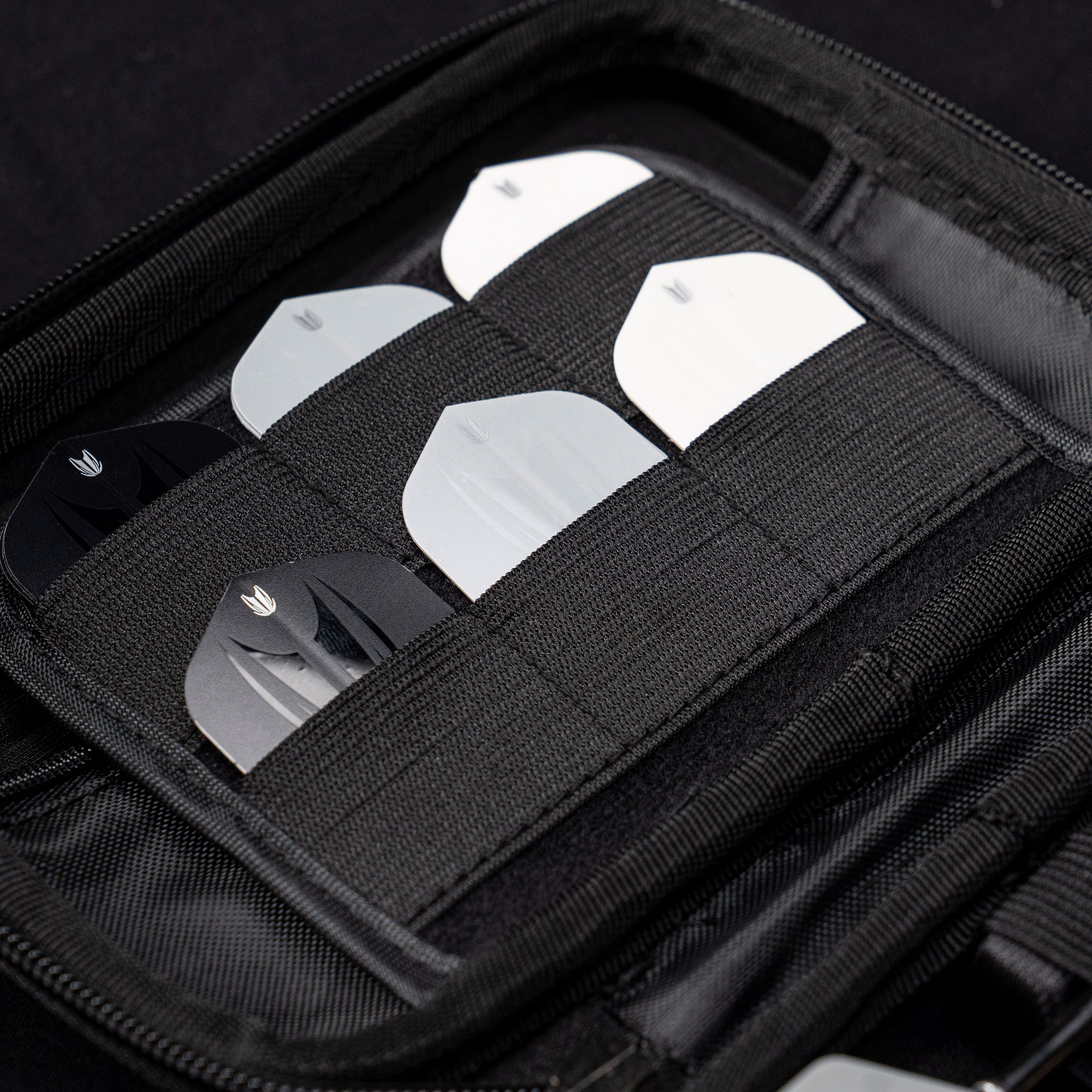 Takoma XL Ghost Series Nathan Aspinall darthoes Das Bild zeigt das „Target Takoma Bolide XL Dartcase“, das mehrere Dart-Flights in schwarzen und weißen Farben organisiert aufbewahrt. Die Flights sind sicher in elastischen Halterungen im Inneren des schwarzen Etuis verstaut.