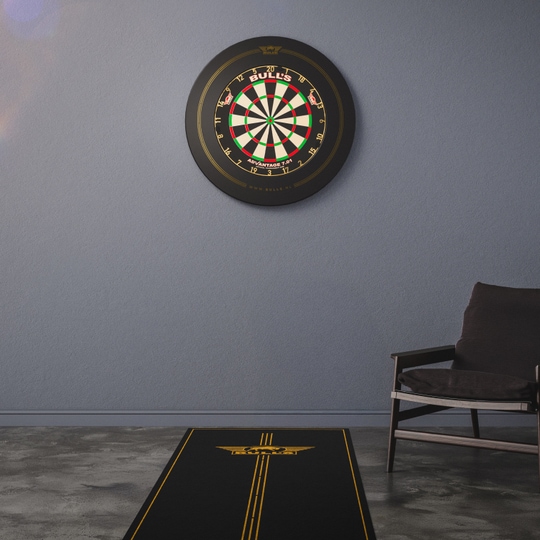 Das Bild zeigt ein Bulls NL Advantage Dartteppich vor einer Dartscheibe an der Wand. Daneben steht ein moderner Stuhl in einem schlicht eingerichteten Raum.