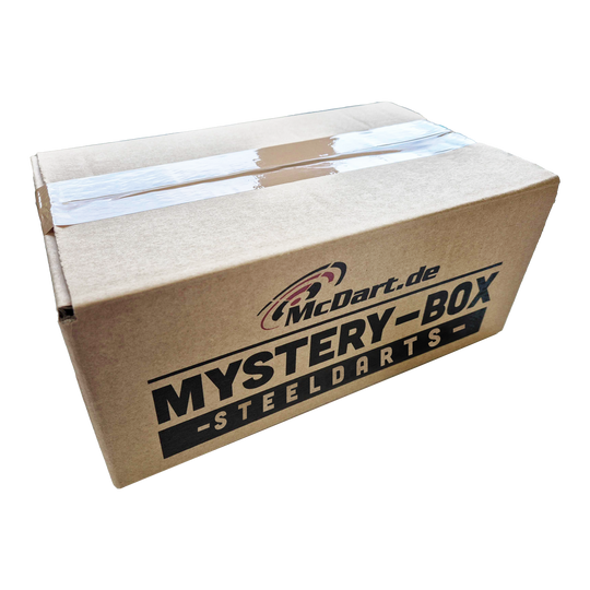 Auf dem Bild ist ein Karton mit der Aufschrift "McDart.de Mystery-Box - Steeldarts" zu sehen. Die Box ist oben mit Klebeband verschlossen.