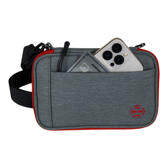Harrows Smart Case XL dart portemonnee Das Bild zeigt eine graue Tasche mit rotem Rand und einem schwarzen Gurt. In der Vordertasche stecken ein Smartphone und eine Kreditkarte.