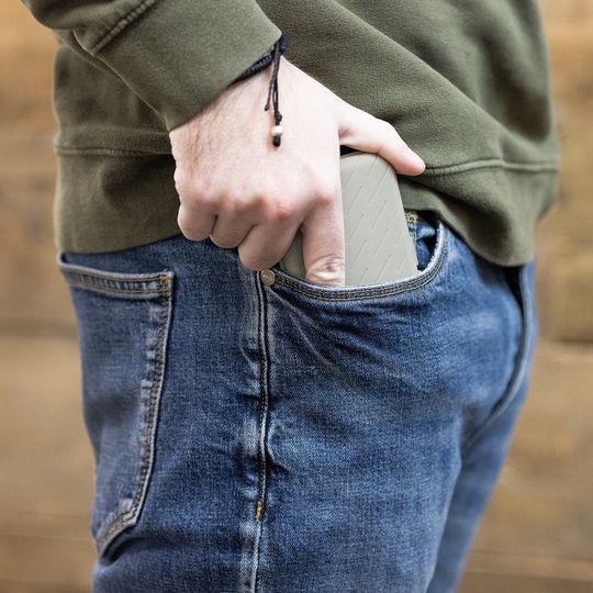 Harrows Slimcase Dart Case Eine Person steckt eine graue Darttasche in ihre Hosentasche. Die Person trägt eine blaue Jeans und einen olivgrünen Pullover.